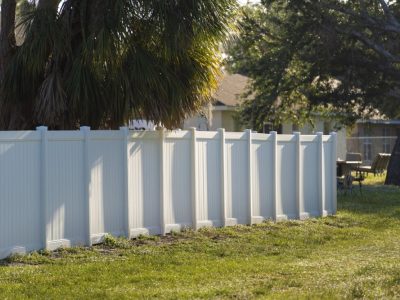 White Vinyl Picket Fence On Green Lawn Surrounding Property Grounds For Backyard Protection And Privacy